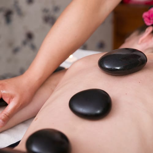 Femme couchée sur le ventre avec des pierres noires posées sur le dos, une autre personne la masse.